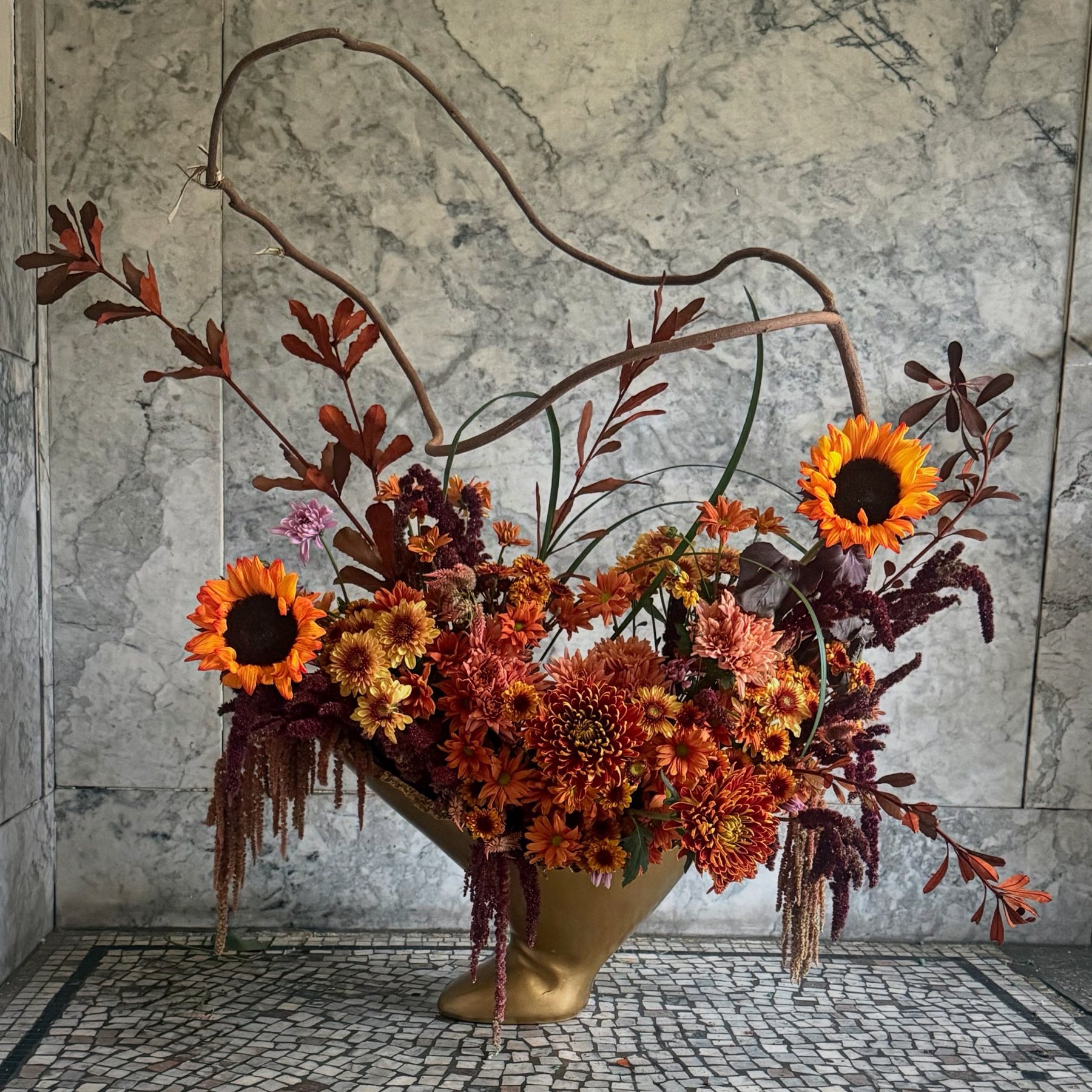An arching vine reaching above an autumnal floral composition